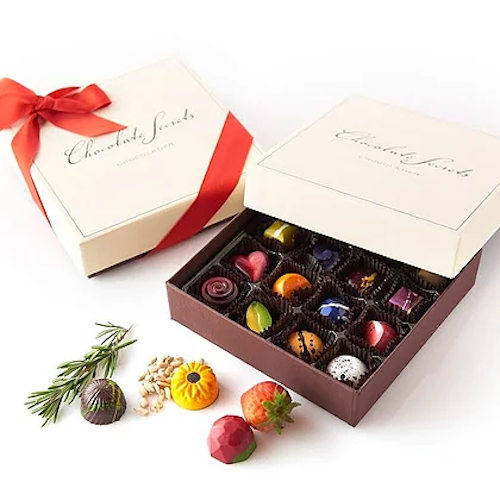 an assortment of colorful chocolates in a white chocolate secrets box with a red ribbon